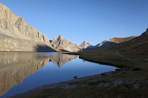 Le lac de l'Oronaye au petit matin, les falaises se reflétant dans l'eau calme, le sentier longeant la rive
