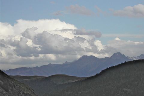 Crêtes bleutées sous un grand nuage, au-delà d'un vallon boisé